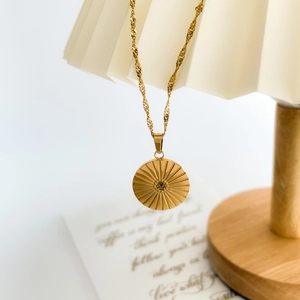 Macro detail of sunburst pendant necklace in 18k gold finish on pleated fabric