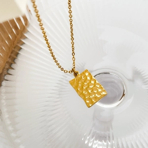 Detail of gold rectangular hammer-textured pendant with fine O-chain on glass
