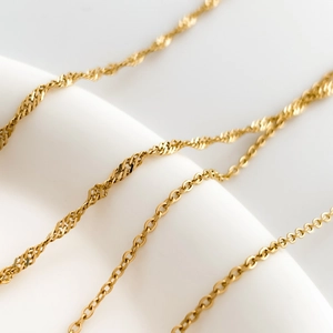 Detail of 18k gold plated water-wave and cable chains on white geometric display