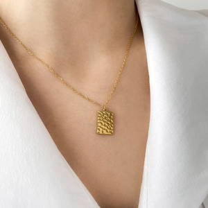 Close-up of golden hammered rectangle pendant necklace worn on a white shirt