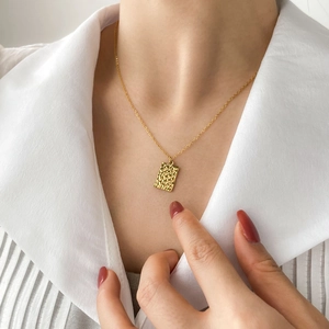 Close-up of a gold rectangular hammered texture pendant necklace on a white shirt