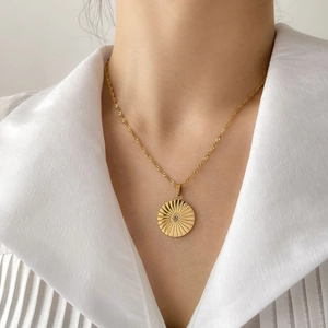 Macro detail of sunburst pendant with crystal on wave chain necklace in 18k gold