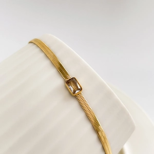 Detail of gold herringbone snake chain featuring a rectangular green zircon gemstone