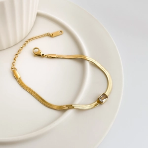 Close-up of gold snake bone chain necklace featuring a rectangular green zircon pendant