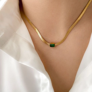 Close-up of a gold flat snake chain necklace with a rectangular green zircon pendant