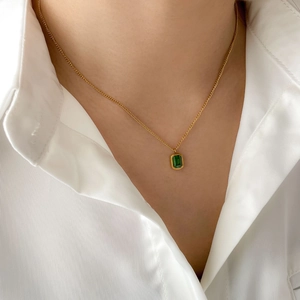 Detailed close-up of emerald green rectangular zircon pendant on a gold chain necklace