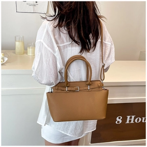Detail van bruine leren tote bag met litchi-patroon, schouderband en rond handvat