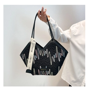Detailed close-up of colorful wave embroidery and logo plate on a black quilted tote bag