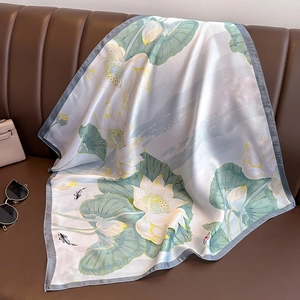 Elegant lotus and koi print silk square scarf draped on a leather sofa with accessories
