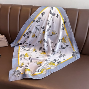Carré en soie satiné à imprimé floral jaune sur fond blanc drapé sur un canapé marron