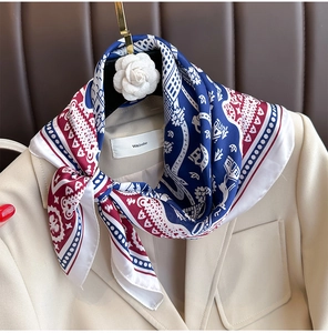 Elegant silk-like scarf with blue and red geometric prints tied on a beige blazer collar