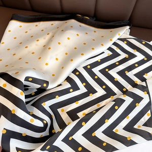 Gros plan d'un foulard en soie à pois oranges et motifs chevrons avec des bordures noires