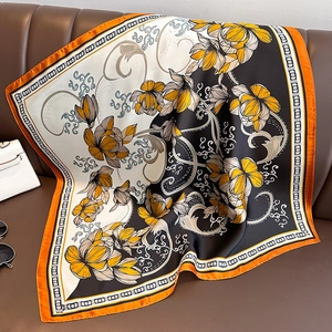 Detail eines Seidensatin-Quadrat-Tuchs mit gelben Blumen auf einem Ledersofa