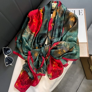 Elegant emerald green silk scarf with large red floral patterns on a stylish hanger