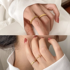 Stacked golden textured rings with braided patterns and cross charms on a white fabric background