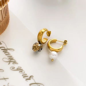 Detail of asymmetric gold C-hoop earrings featuring a brown crystal and white pearl