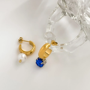 Detail of gold asymmetric hoop earrings with a white pearl and a blue crystal pendant
