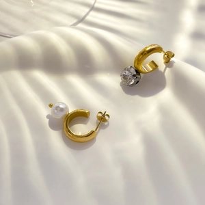 Detail of asymmetric C-shaped gold earrings with white pearl and clear crystal accents