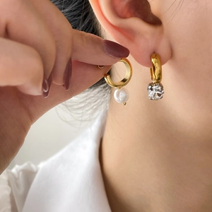 Asymmetric gold hoop earrings featuring a white pearl and a clear crystal pendant