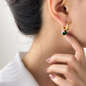 Detail of gold C-hoop earring featuring a faceted dark green gemstone on model