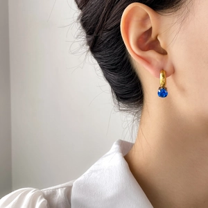 Asymmetric C-shaped gold earring with blue gemstone worn by a model in soft light