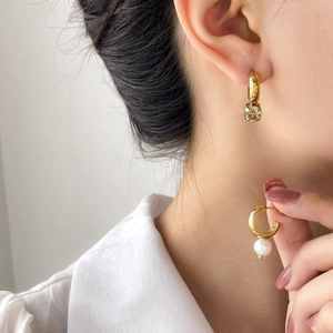 Detail of asymmetric gold earrings with champagne crystal and white pearl charms