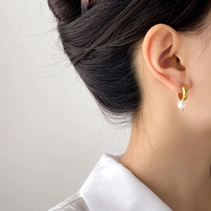 Close-up of a model wearing a thick gold hoop earring with a white pearl pendant