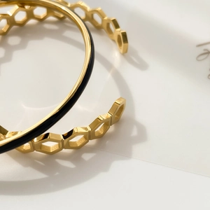 Close-up of gold honeycomb cutout bangle and black enamel slim open bracelet set