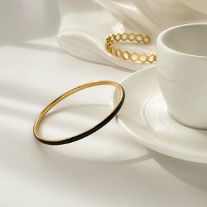 Close-up of minimalist gold bangle with black enamel finish on soft satin silk fabric