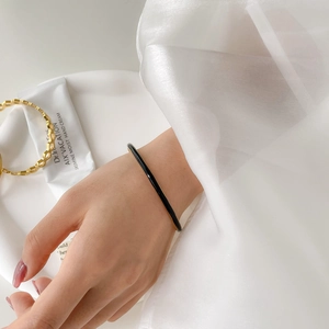 Detail of minimalist black enamel and gold bangle worn by a model in a luxury setting