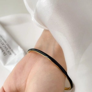 Close-up of minimalist black enamel and gold slim bracelet on wrist with silk cuff