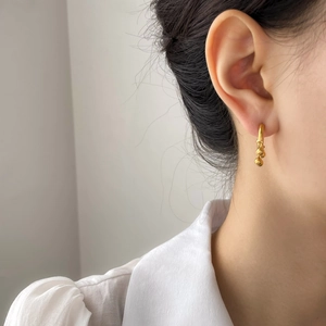 Macro detail of gold geometric hoop earrings with triple graduated beads on a model