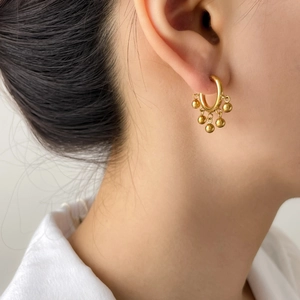 Elegant gold hoop earrings with polished metal bead charms shown on a female model