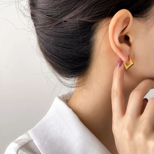 Detail of a minimalist gold square hoop earring with a matte finish on a female model