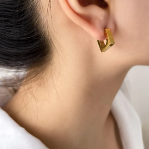 Close-up of a polished gold geometric square earring worn on a female earlobe