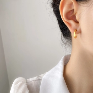 Close-up of a minimalist hexagonal gold earring worn on ear with white shirt background