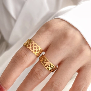 Detail of two gold geometric hollow rings featuring lace and diamond patterns on finger