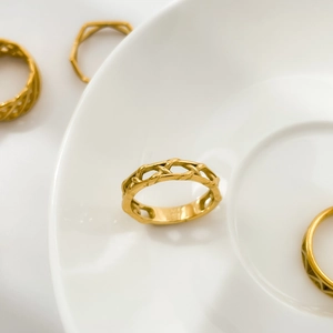 Close-up of golden geometric woven rings with hollow diamond lace textures on white ceramic