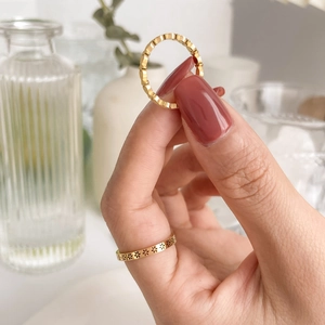 Détail d'une bague dorée gravée de fleurs et d'un anneau ondulé sur main