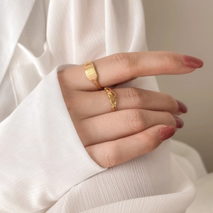 Detailed close-up of golden signet ring with geometric patterns and hollow leaf band ring