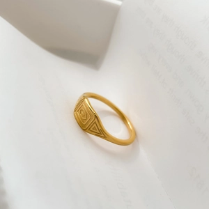 Detailed close-up of a gold signet ring with engraved geometric patterns on white paper