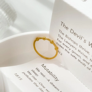 Detail shot of a minimalist gold beaded ring resting on white ceramic with soft shadows