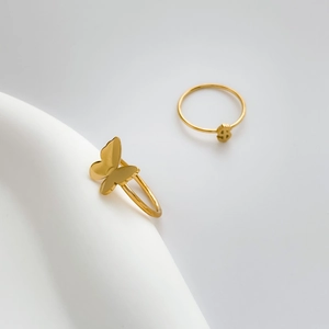 Detail of vintage gold butterfly and dollar sign rings on white geometric stands