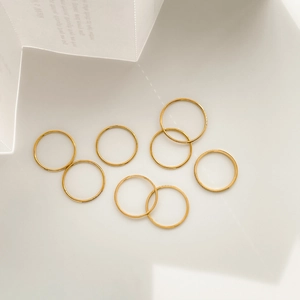 Artistic layout of eight minimalist thin gold stackable rings on white paper background