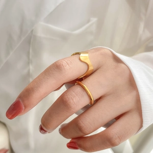 Détail d'une bague vague dorée et d'un anneau minimaliste portés avec un revers de chemise blanc