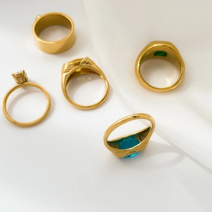 Detailed view of five gold-plated rings with colorful zircon gems on white silk background