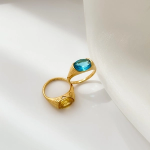 Close-up of gold-plated rings with large oval blue and amber zircons on white silk