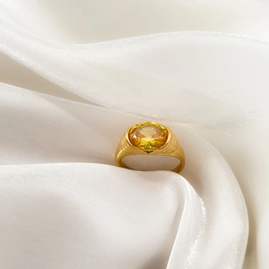 Detailed view of an oval yellow gemstone ring on a white silk background