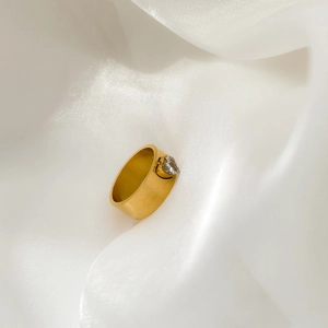 Detail of a wide gold ring with a heart-shaped zircon on white silk background
