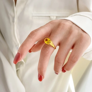 Detail of gold ring with yellow oval gemstone and textured band worn on hand